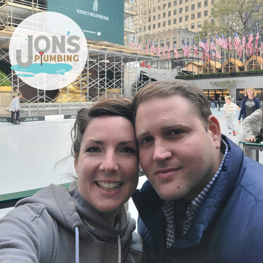 Jon's Pic Jon from Jon’s Plumbing and his wife smiling together at the Rockefeller Center ice rink in New York City, with American flags and scaffolding in the background. The Jon’s Plumbing logo is overlaid in the corner.